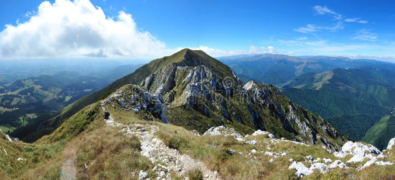 Landscape shot of Piatra Craiului National Park with a dusting of snow, captured during early morning light. Show a small group of people with a guide following tracks. Focus on the vastness of the landscape and the rugged beauty of the mountains.
