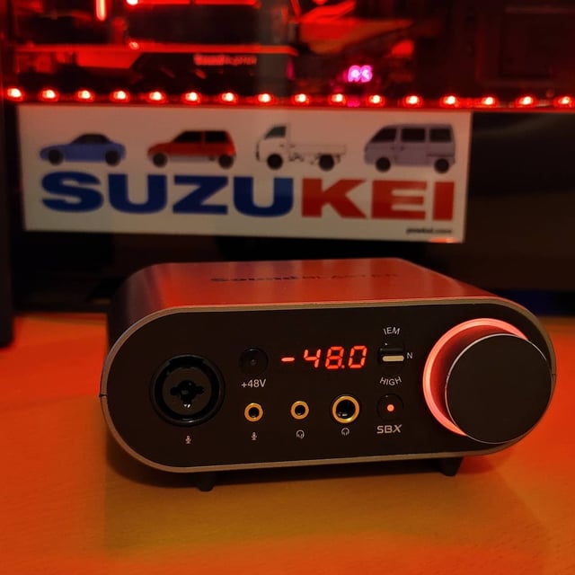 Close-up of the AE-9's Audio Control Module, highlighting the XLR input, headphone jacks, volume knob, and OLED display.