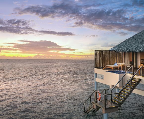 Exterior of a Maldives overwater bungalow at sunset, with warm lighting and a tranquil atmosphere