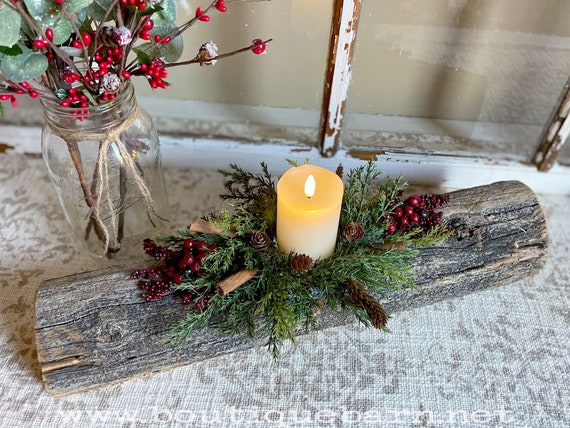 A Yule beeswax candle centerpiece radiantly burning on a dark wood surface with greenery, pine cones and a dark background.