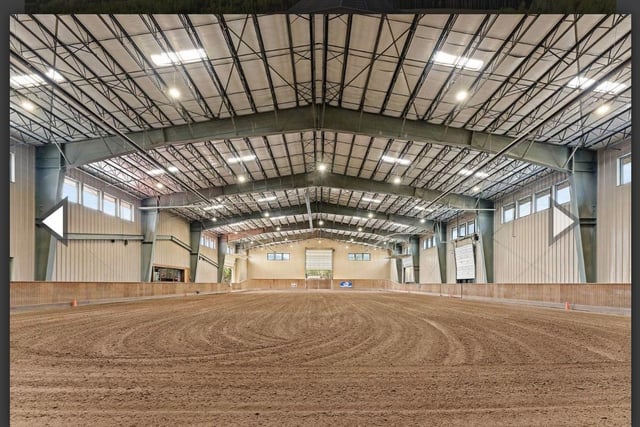 A large indoor space, possibly a repurposed riding arena, featuring natural light and a rustic atmosphere.