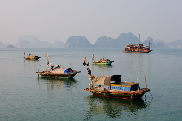 Wide angle shot of Ti Top Island, showing tourists swimming in the clear turquoise waters at the base of the island, with boats anchored nearby