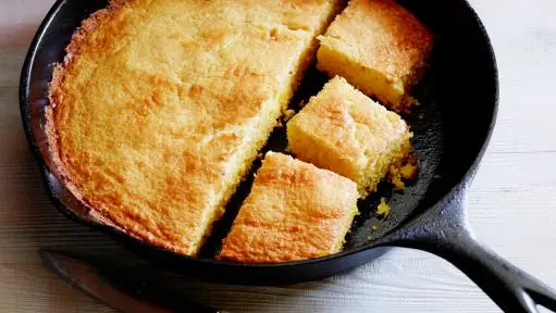 Image showing a hand rolling out the cornmeal crust dough on a floured surface with a rolling pin, preparing it for the tart pan.