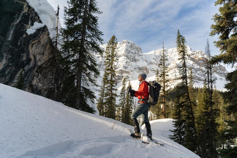 A couple snowshoeing through a snowy forest in the Canadian Rockies. The sun is shining and the snow is sparkling.