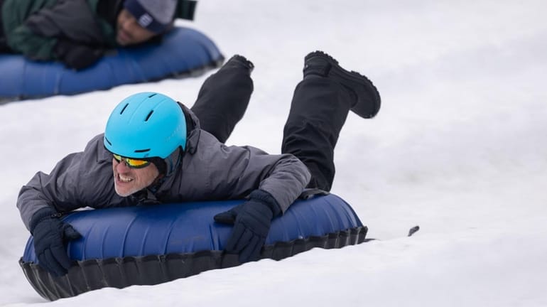 People sledding down Mount Vogel on traditional wooden sleds, with smiling faces and snow-covered scenery