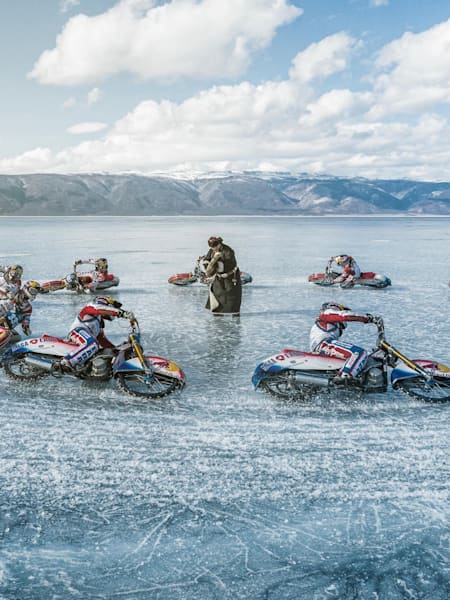 Ice speedway motorcycles lean into a turn on the frozen surface of Lake Baikal, ice spraying from studded tires in a dynamic display of speed.