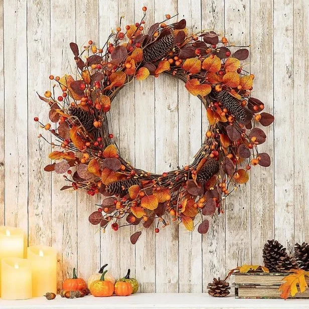 A pinecone and berry wreath hangs on a dark wooden door