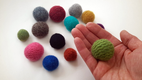 Hands cutting up an old, felted wool sweater into strips on a wooden table.