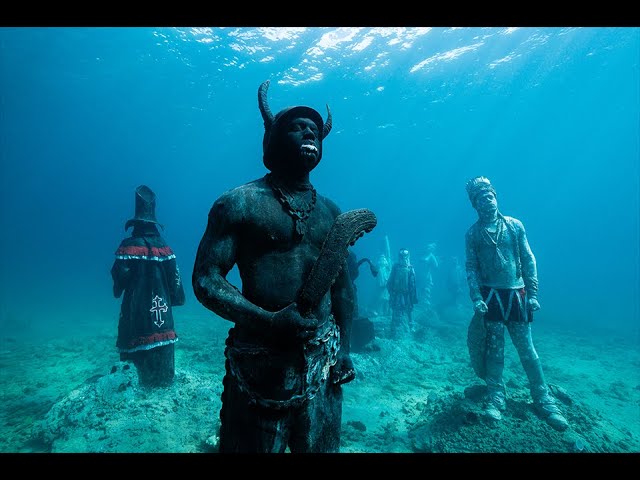 A diver glides effortlessly through the Grenada Underwater Sculpture Park, showcasing the vibrant coral growth and diverse marine life inhabiting the sculptures.