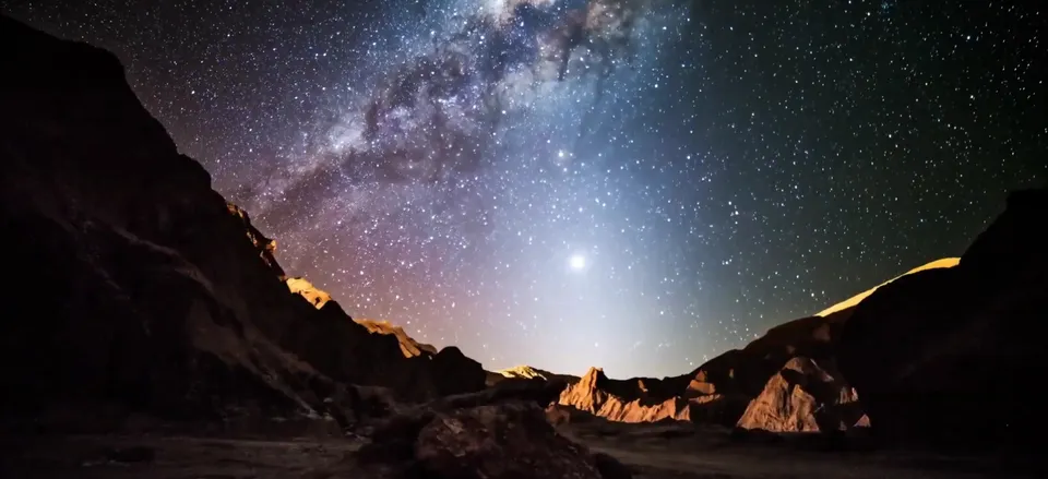 The Atacama Desert landscape at night under a sky full of stars, with silhouetted mountains in the background