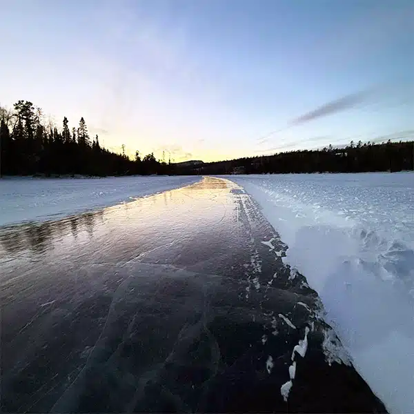 Close-up of a hand holding a freshly caught fish, glistening in the firelight against the backdrop of a snow-covered riverbank, captured with a shallow depth of field.