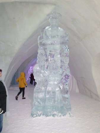An illuminated bedroom inside the Hôtel de Glace, showcasing the ice bed, ice sculptures, and blue lighting