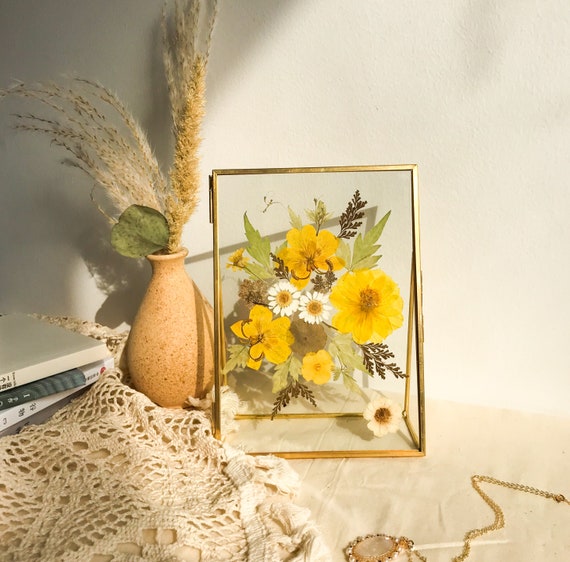A botanicalcore-inspired living room with framed pressed flower art displayed on a linen wall alongside vintage botanical prints, dried herb bundles, and natural textures like linen and burlap.