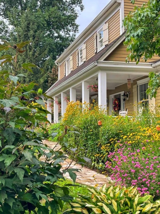 a porch with mums and other fall plants in rustic containers