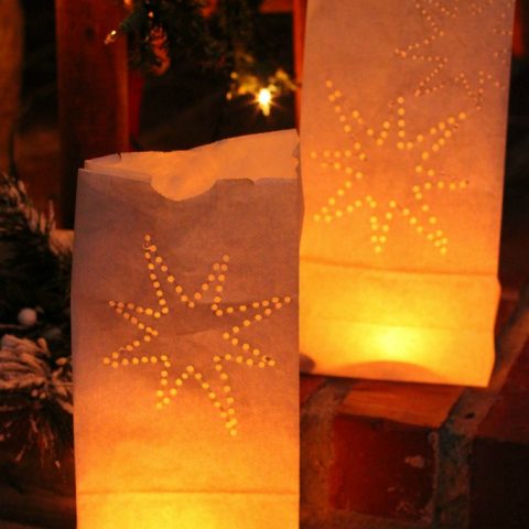 Close-up hands cutting star shapes into a brown paper bag for a luminary. Winter solstice craft project.