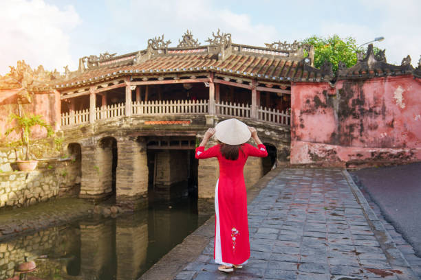 Anya in a red ao dai, posing gracefully in front of the iconic Japanese Covered Bridge, capturing the beauty of Vietnamese culture.