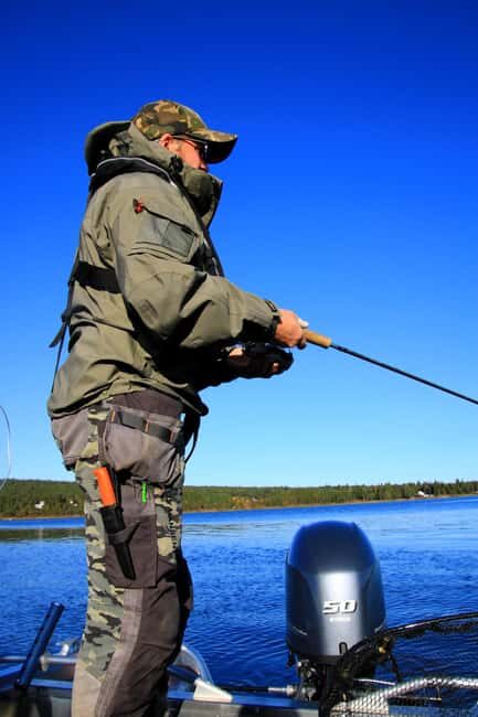 An angler sits patiently on a frozen lake near Kelowna, ice fishing while bundled in warm Arc'teryx apparel, representing a sustainable and peaceful winter activity.