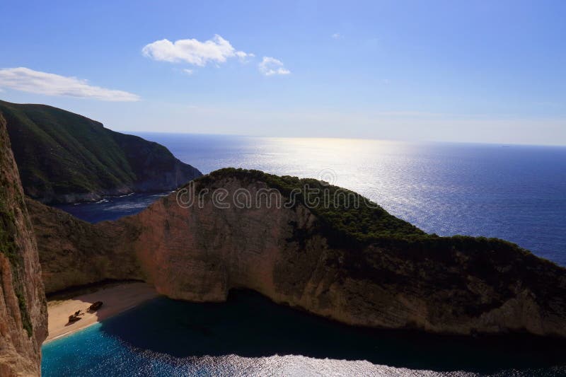 A panoramic shot of Navagio Beach from the cliffs above, capturing the turquoise water, the shipwreck, and the dramatic cliffs. Another image from the water level emphasizing the height of the cliffs.