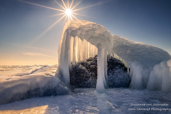 A close-up shot of a half-full pint glass filled with a light amber-colored beer, set against a blurred background of a rustic bar or brewery. Foam clings to the inside of the glass, and condensation droplets are visible on the outside, suggesting a cold beverage. The overall ambiance is warm and inviting, typical of a Northwoods establishment.