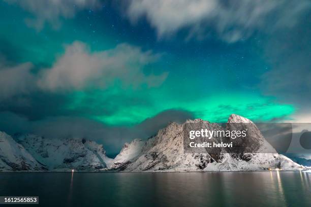 A stunning, long-exposure photograph of the Northern Lights reflected in the snow, with a silhouetted snowshoer in the foreground