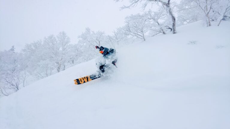 Backcountry snowboarder descending a powder-covered slope in Hokkaido, alt text: A snowboarder carves through deep powder on the slopes of Mount Yotei, showcasing the legendary snow conditions of Hokkaido, Japan.
