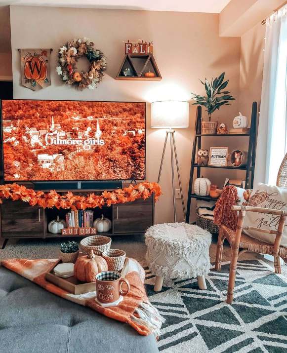 A collection of candles in glass jars and pumpkins are arranged on a rustic wooden surface, providing warm lighting and autumnal scents.