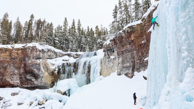 A climber silhouetted against a wall of blue ice. Frozen waterfalls cascade down the canyon walls, creating a dramatic scene. This image captures the beauty and the challenge of ice climbing.