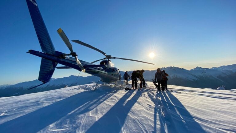 Point-of-view shot from inside a helicopter, showing the vast backcountry terrain of British Columbia below.