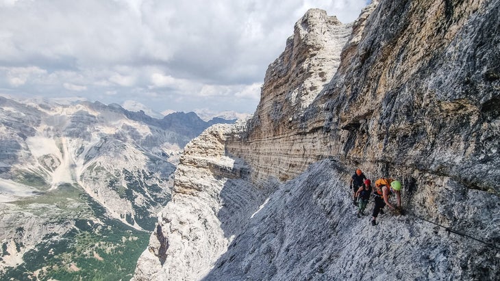 A couple scaling the Via Ferrata Ivano Dibona in the Dolomites, showcasing the steel cables, dramatic cliffs, and the turquoise Sorapiss Lake below.
