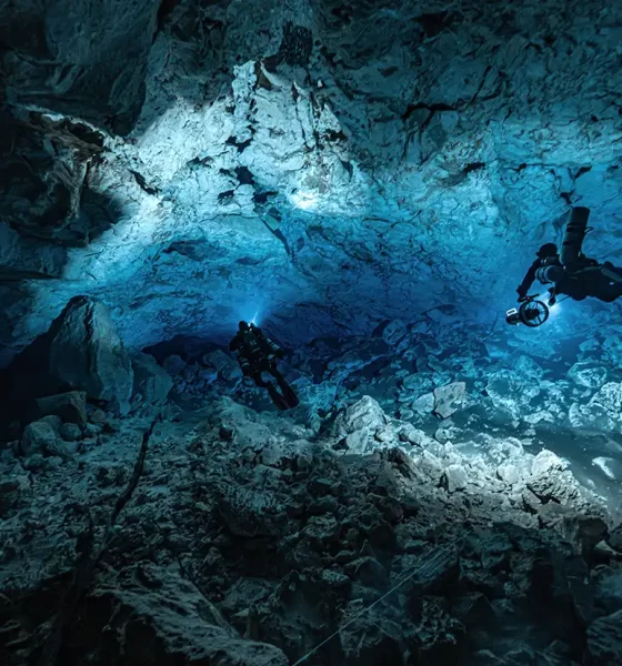 Christina Zenato demonstrating proper hand signals during a cave diving expedition in a cenote, showcasing her expertise and calm demeanor.