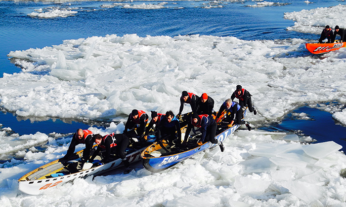 Ice canoeing on the St. Lawrence River, showing participants paddling through icy waters with Quebec City in the background