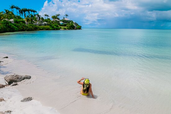 An overhead shot of Valley Church Beach, showing the calm turquoise waters and white sand, with lush green hills surrounding the beach.