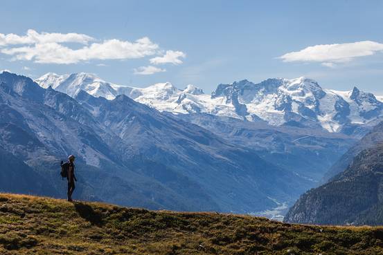A snow-capped mountain range with a hiker standing on a rocky outcrop, enjoying the vast view. This scene encapsulates the sense of accomplishment and breathtaking beauty that mountain hiking offers, encouraging readers to experience it firsthand.