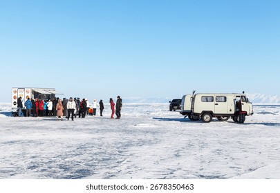 A fisherman drilling through the thick ice of Lake Baikal, surrounded by snow and vast expanse of frozen lake
