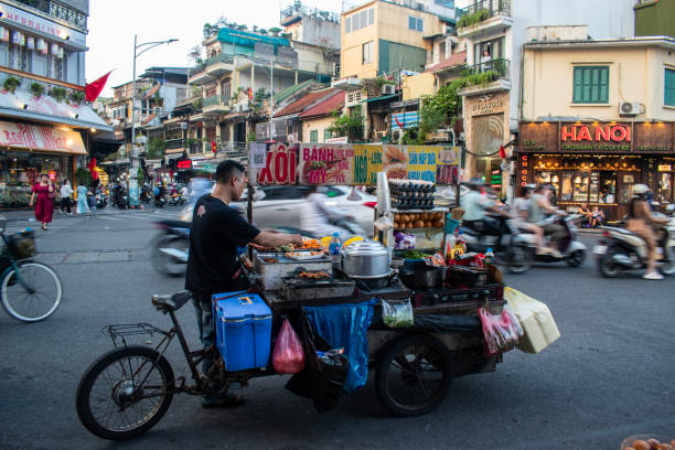 A Vietnamese man cooking food to sell on his wheeled cart in the middle of the crowded street