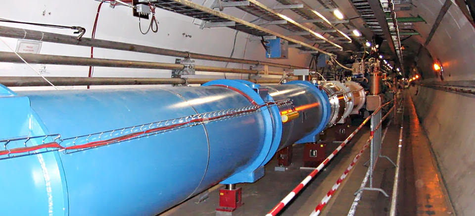 A complex visualization of the Large Hadron Collider (LHC) is shown. The LHC appears as a massive, circular structure with intricate networks of tunnels and detectors. Streams of particles are colliding at various points within the collider, creating bursts of energy and light. The overall impression is one of immense power and scientific complexity.