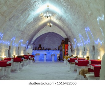 Interior shot of the Ice Hotel bar, showcasing elaborate ice carvings and guests enjoying drinks. Low-light photography emphasizing the cool, blue tones of the ice. Add motion blur for liveliness.