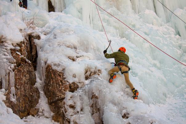 A climber mid-swing with their axe, illuminated dramatically against the ice in Ouray Ice Park