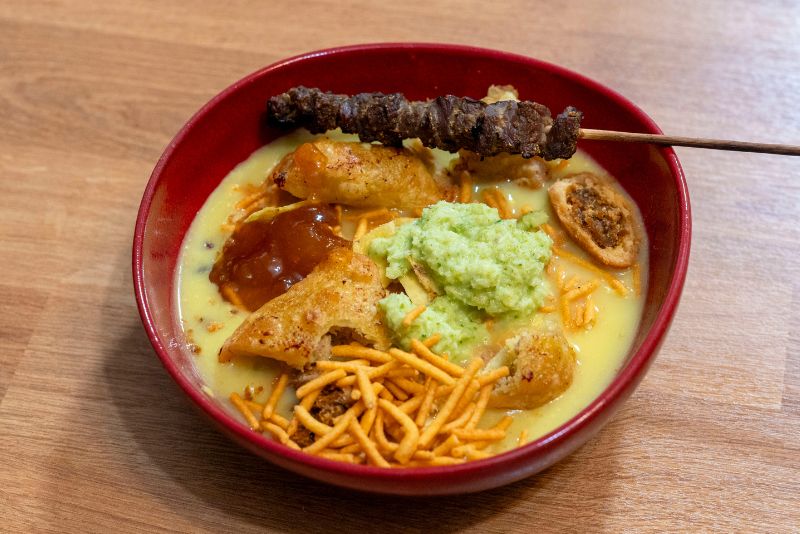 A stunning aerial view of a pristine white-sand beach in Zanzibar, fringed with palm trees and surrounded by turquoise waters. A traditional dhow sailing boat is visible in the distance.