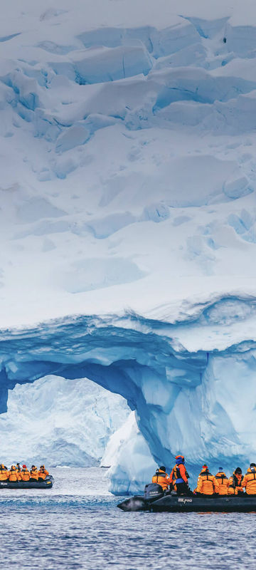 A wide-angle shot of a cruise ship sailing through icy waters with towering icebergs in the background.