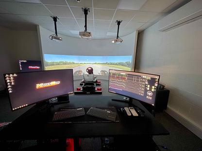 A behind-the-scenes shot of the simulation setup with a gamer immersed in the game, showcasing the multi-monitor array and racing/flight controls. Focus on the gamer's focused expression and the immersive experience.