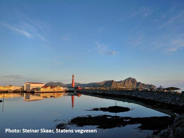 Fat bikers crossing floating bridges in Flåm, Norway, with snowy mountains in the background.