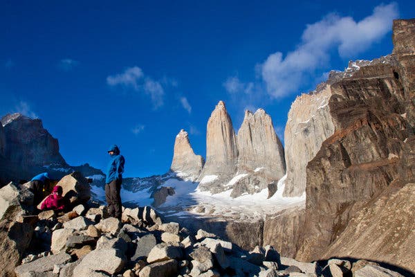 A group practices yoga on a platform overlooking a glacial lake in Patagonia, Chile, surrounded by snow-capped granite peaks and lush forests, illustrating the harmonious blend of physical activity and serene natural beauty.