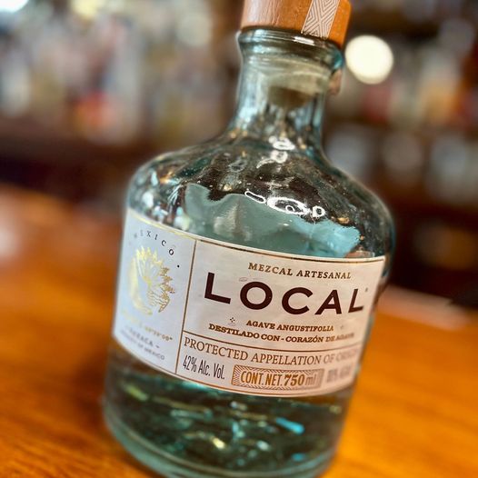 A selection of mezcal bottles and copitas on a wooden bar top