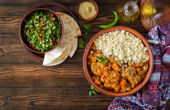 A group of people are gathered around a table in a kitchen, preparing Zanzibari dishes like Zanzibar pizza and Urojo soup during a Swahili cooking class.