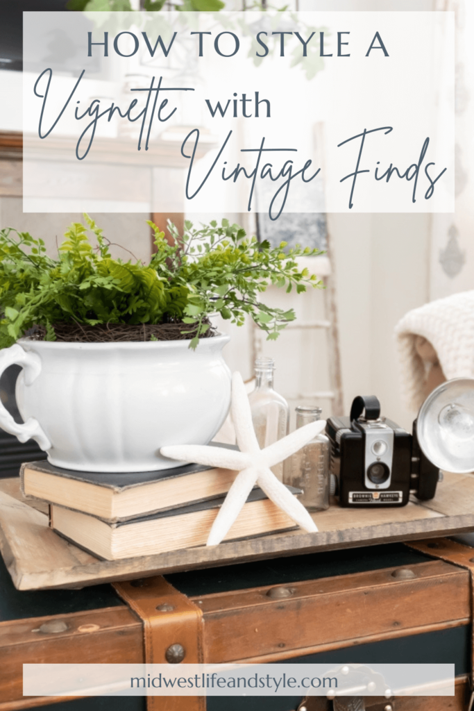 A vignette featuring a collection of thrifted items styled on a farmhouse-style shelf or mantel: antique books, candles, vintage clock, framed botanical prints.