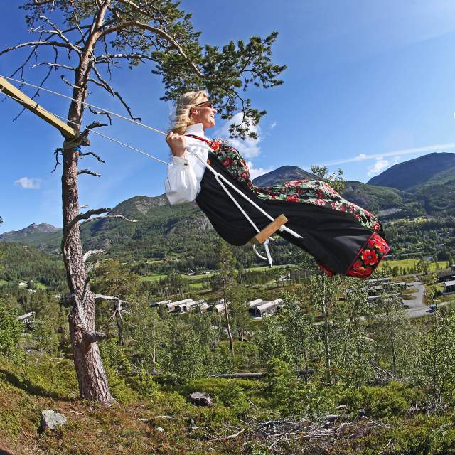 An elderly Norwegian woman in a bunad base jumping from a snowy cliff.