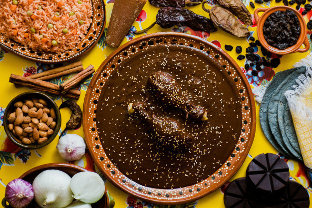 A close-up shot of a traditional Oaxacan woman grinding spices on a metate, showcasing the traditional preparation of Mole Negro.