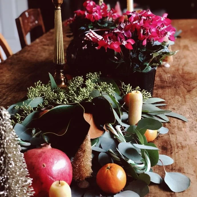Close-up of a partially assembled winter solstice centerpiece showing the layering of branches, berries, and pinecones.