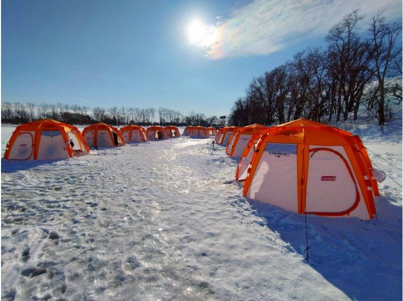 People ice fishing on a frozen lake, surrounded by snow
